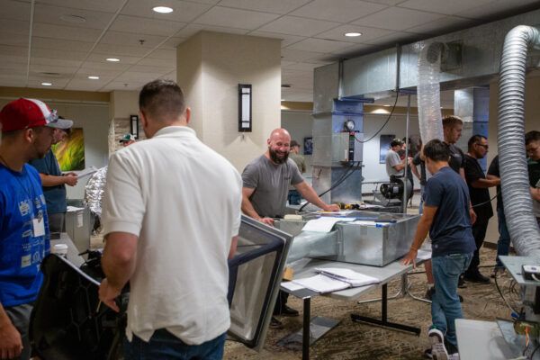 Several people standing around a table, engaged in discussion while examining a large machine.