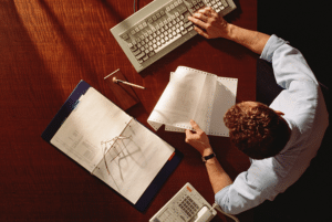 aerial view of a man working on a computer and with budget sheets